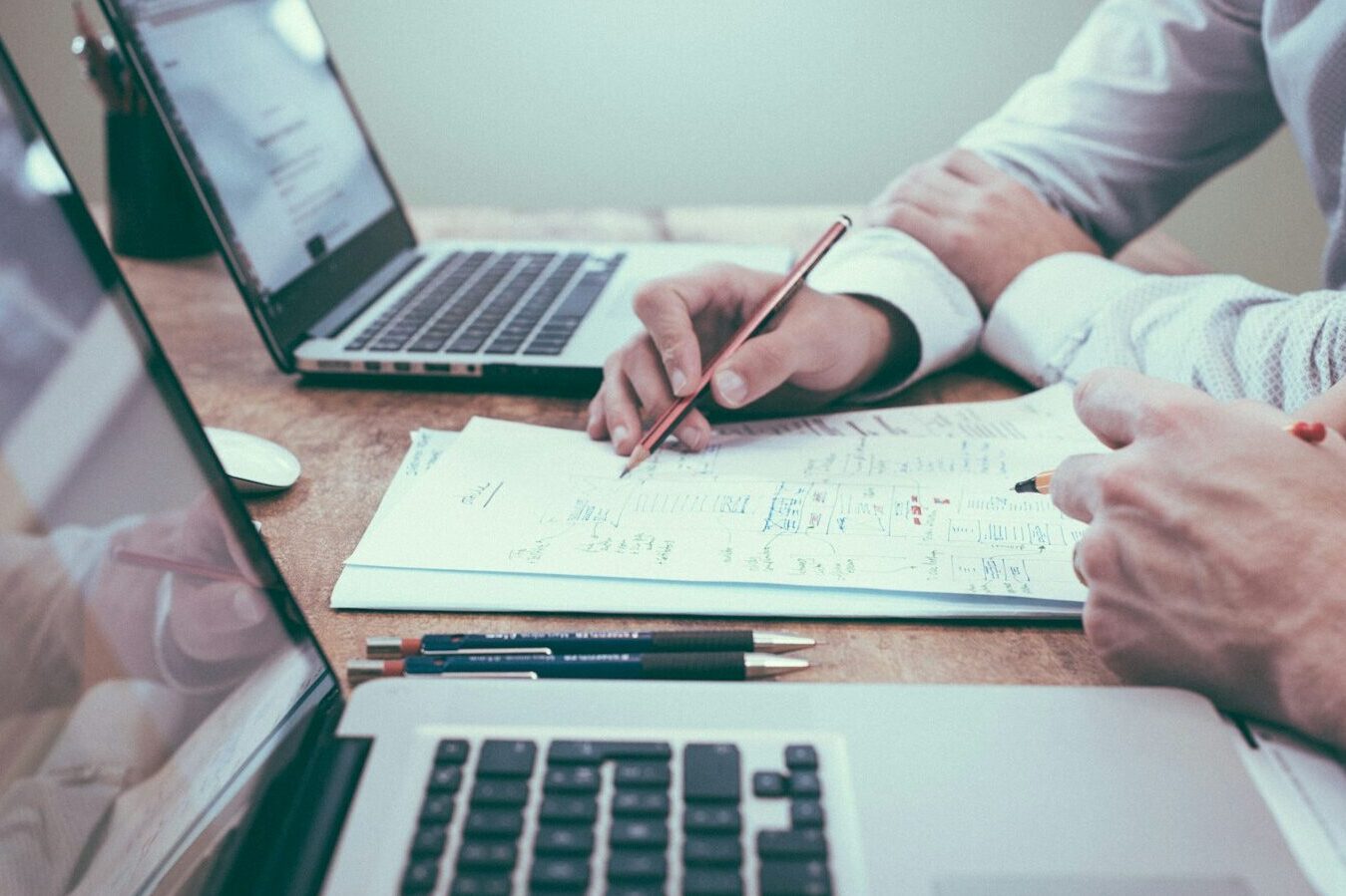 person holding pencil near laptop computer