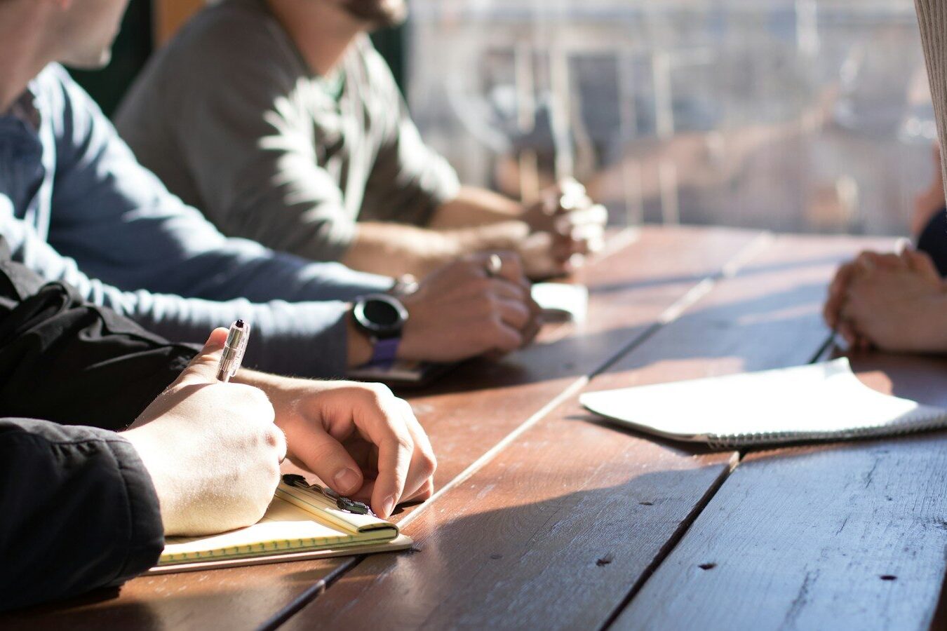 people sitting on chair in front of table while holding pens during daytime